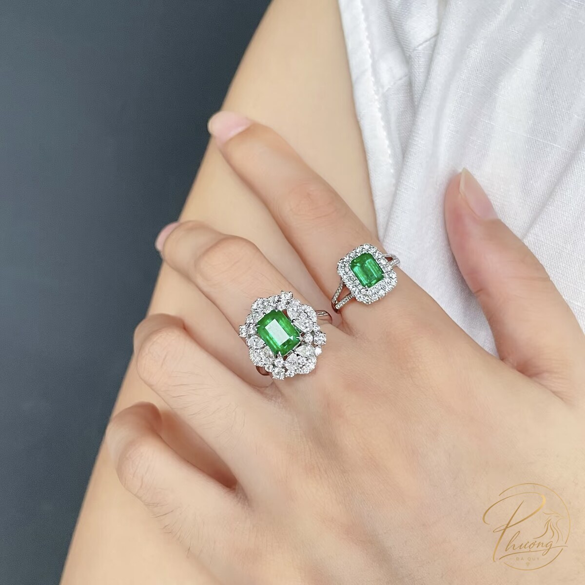 hai nhẫn đính đá Emerald cắt vuông viền kim cương halo đeo trên tay, đá chính của người cung Kim Ngưu