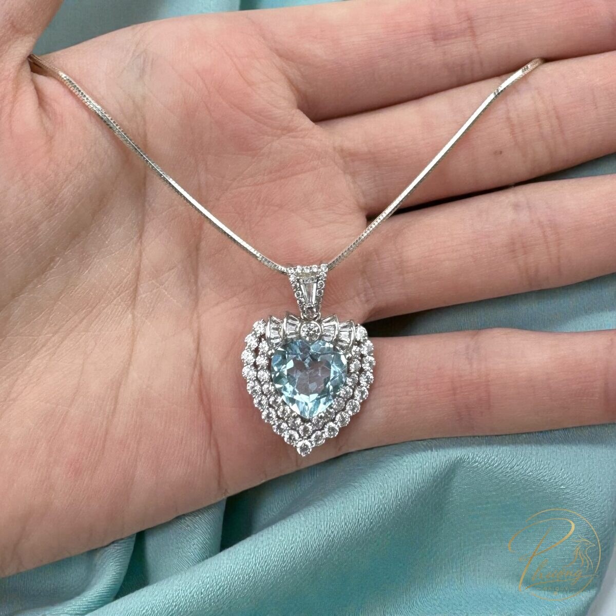 Mặt dây chuyền bạc hình trái tim đính đá Topaz xanh đặt trên lòng bàn tay