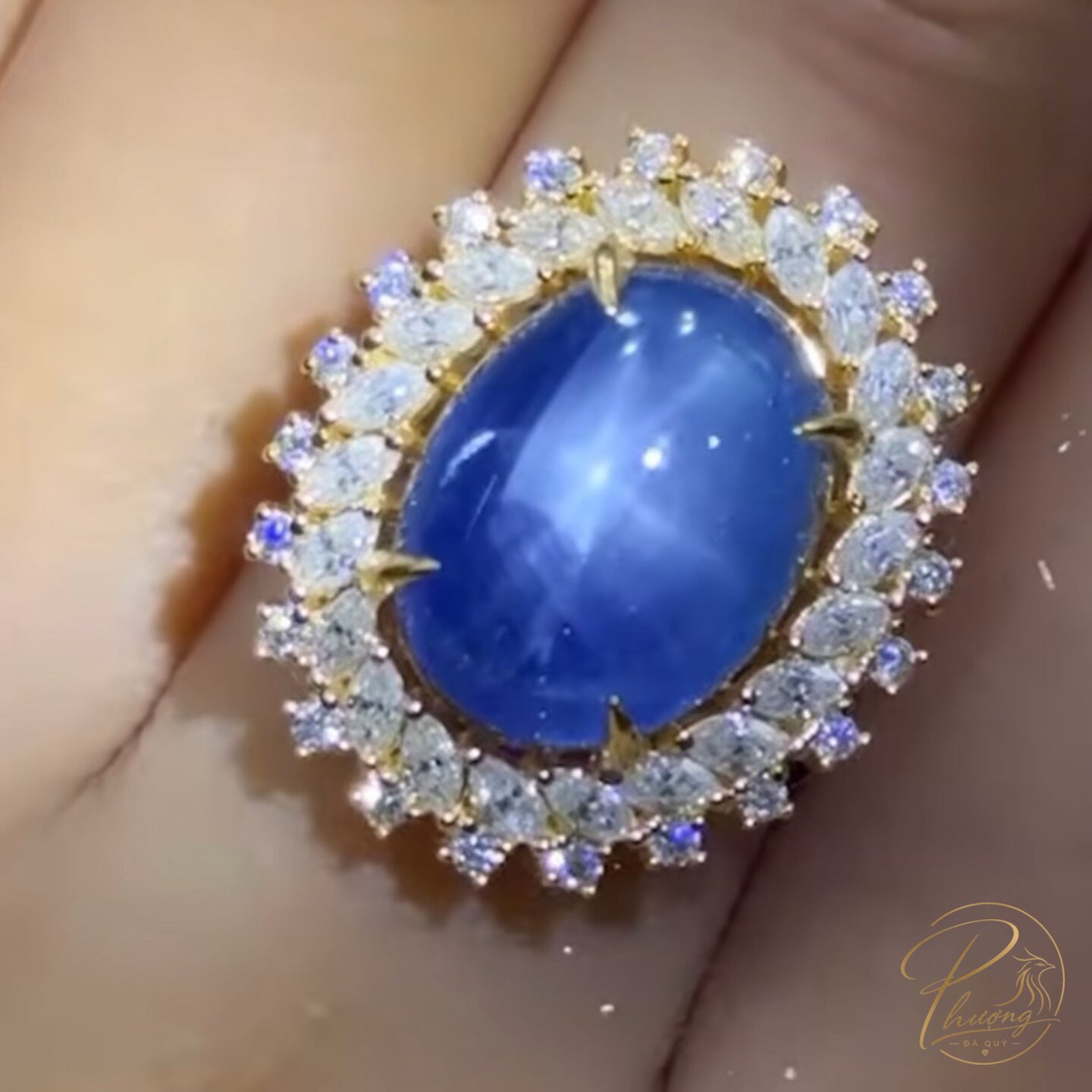 Nhẫn vàng gắn Sapphire lam cabochon hiệu ứng sao, viền halo đá trắng, đeo trên tay