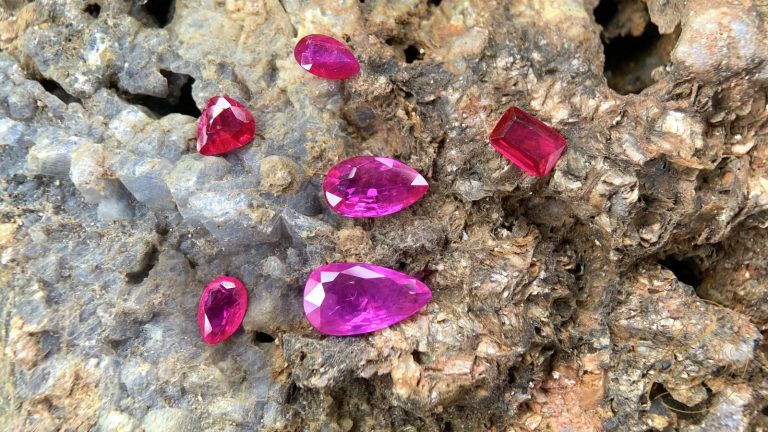 Sáu viên Ruby tự nhiên mài giác, sắc đỏ đến hồng tía, đặt trên khối đá thô