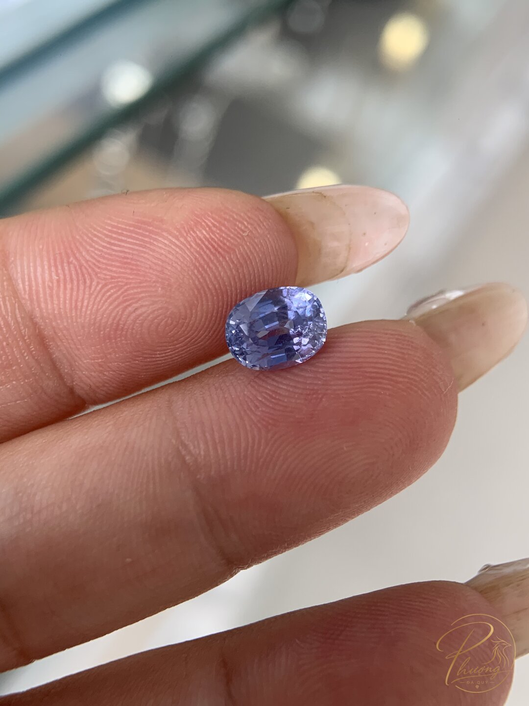 Sapphire tự nhiên mài giác dáng oval màu lam pha tím, cầm giữa hai ngón tay