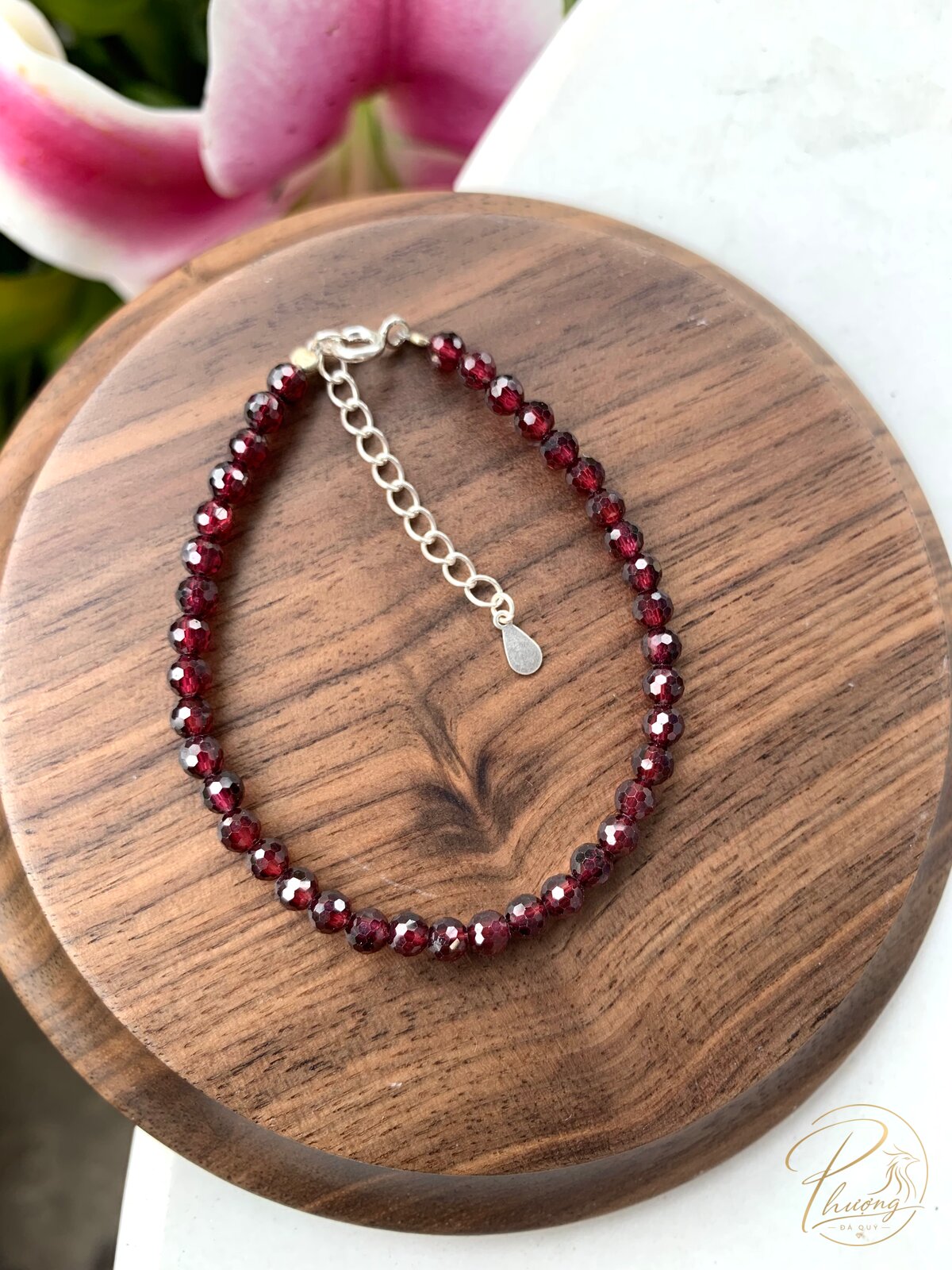 Vòng tay phong thủy Garnet đỏ thẫm hạt mài giác đặt trên đế gỗ óc chó